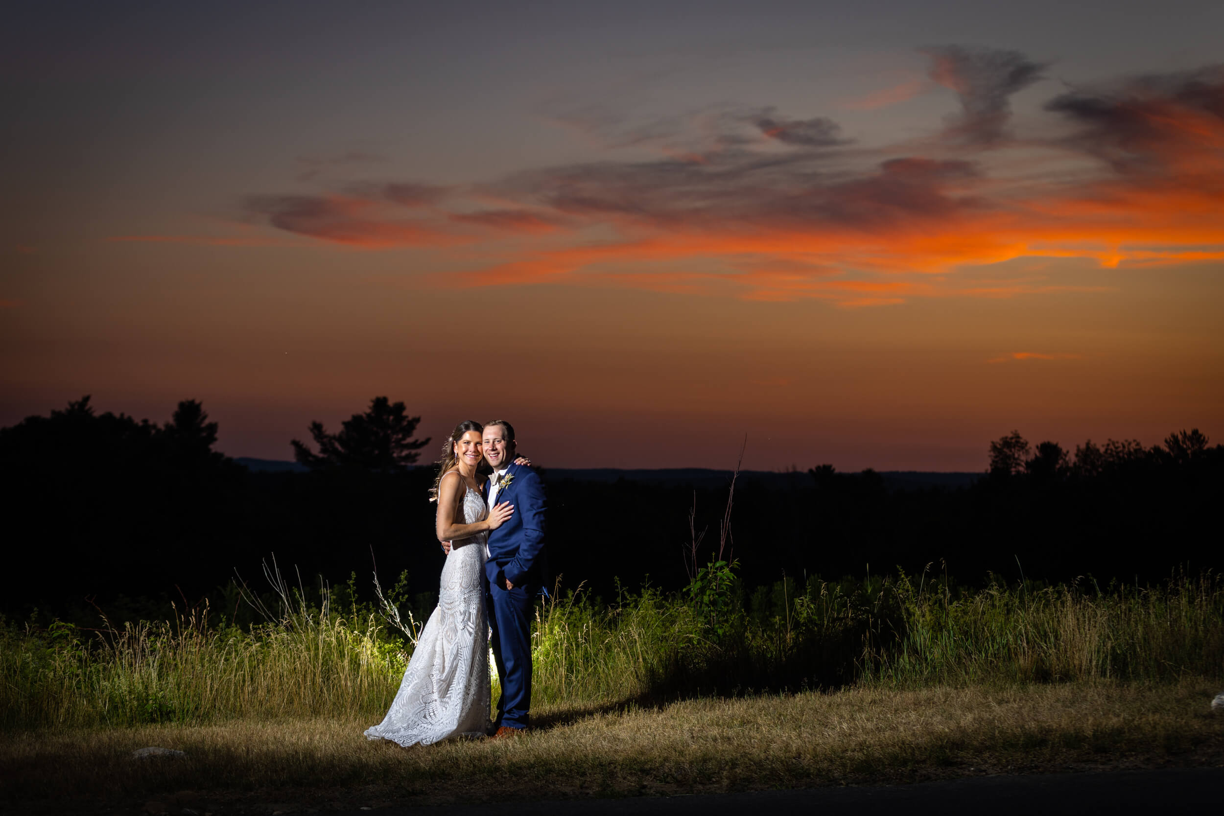 Bride in great gatsby gown and groom in blue suit embracing for vibrant sunset wedding photo at Harrington princeton ma