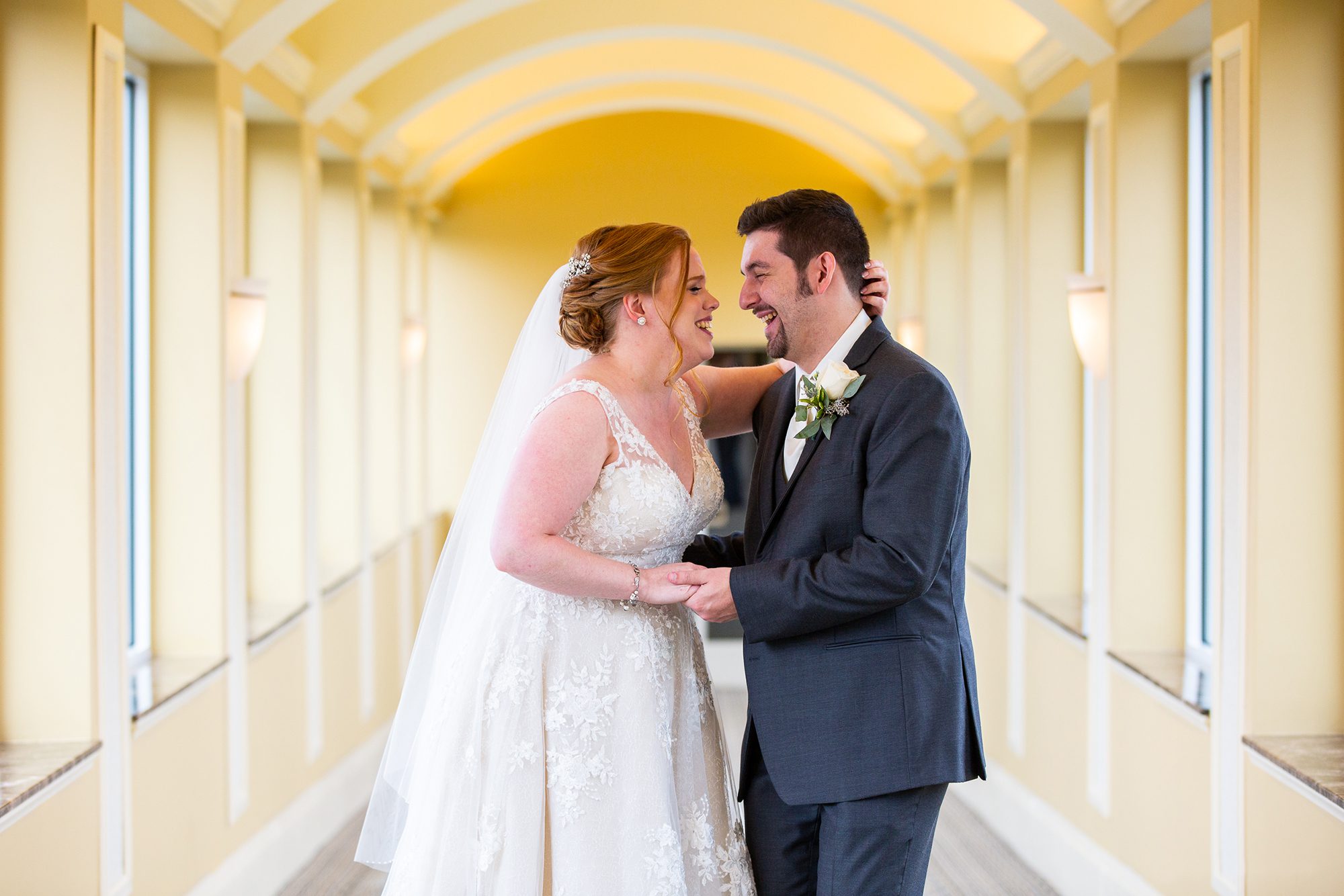 bride-groom-laughing-in-yellow-hallway-devens-common-center-wedding