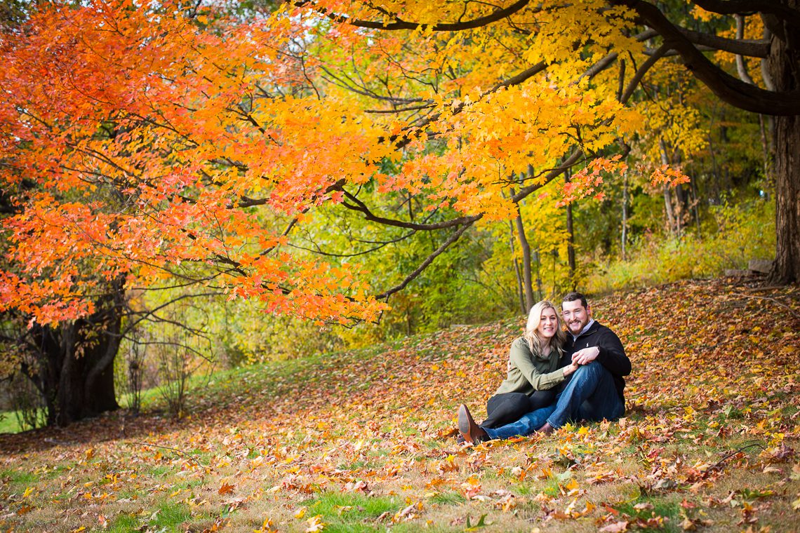 couple-sitting-under-orange-yellow-fall-foliage-seasonal-massachusetts-engagement-photography-idea