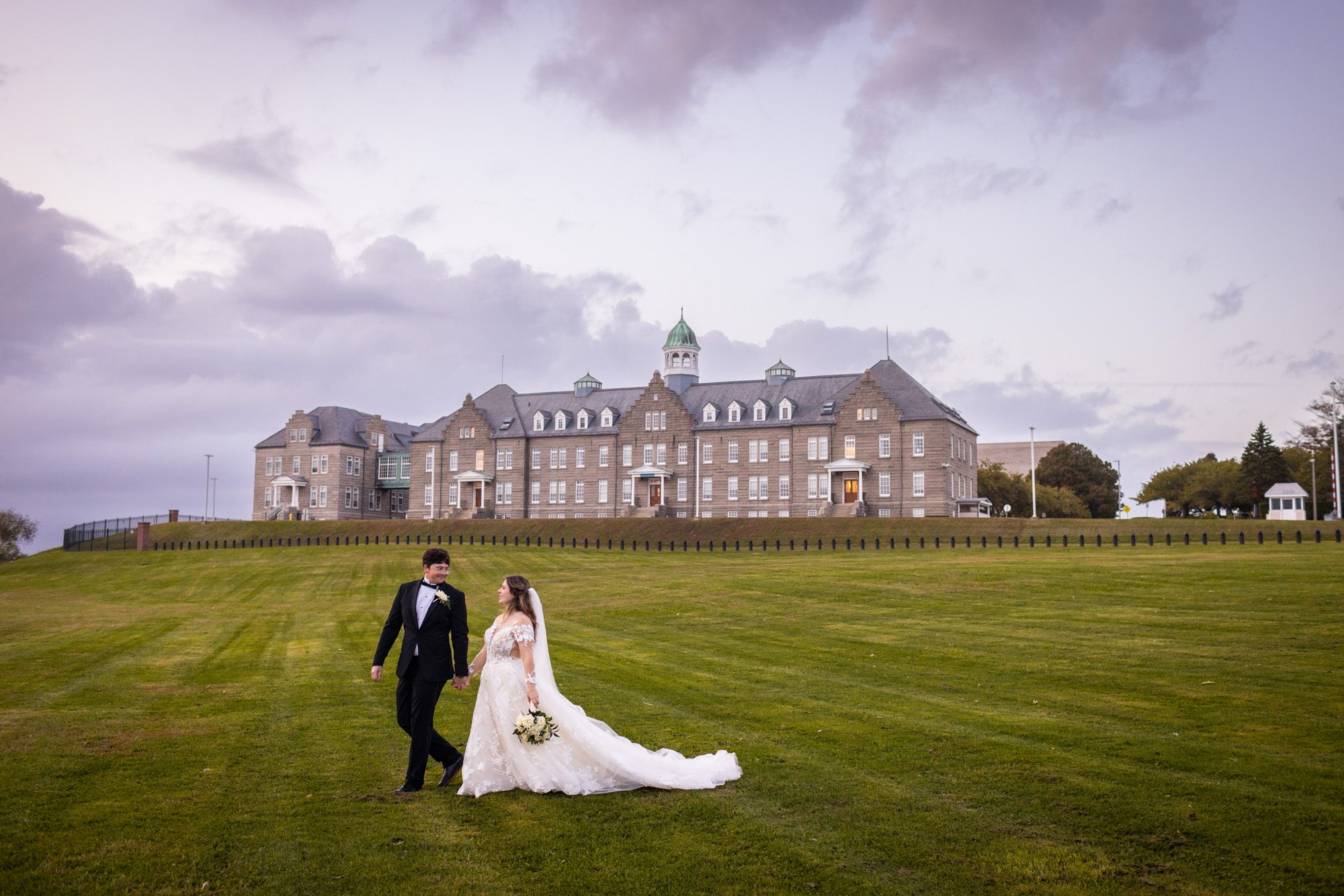 Groom in black tux leads elegant bride across large lawn in front of mansion at newport-ri-wedding-photos-newport-officers-club