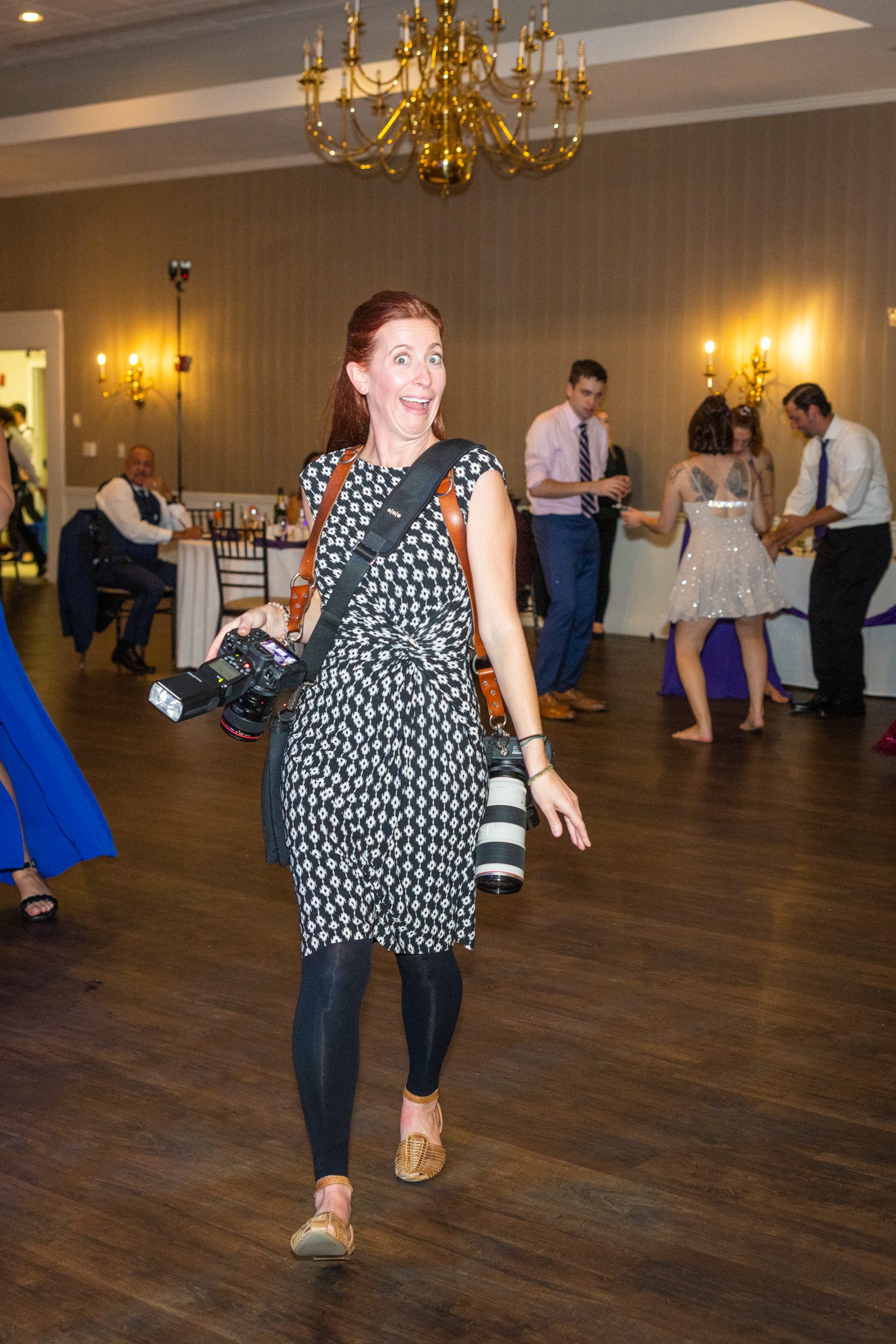 Audrey cutler walking across a dance floor at a wedding carrying two cameras