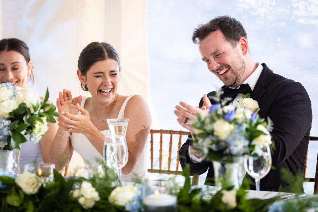 bride and groom clapping and laughing during speeches  at reception How to Plan Your Wedding Without Losing Your Mind 